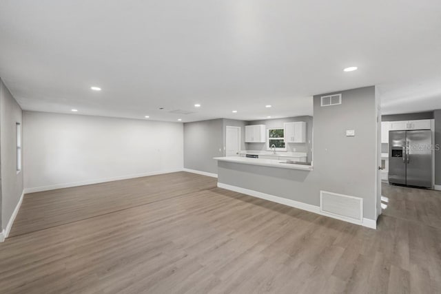 unfurnished living room featuring visible vents, light wood-style flooring, and baseboards