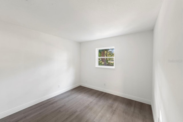 spare room featuring baseboards and dark wood-style flooring