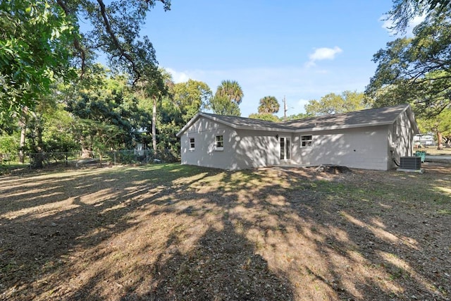 back of house with central AC unit, concrete block siding, and fence