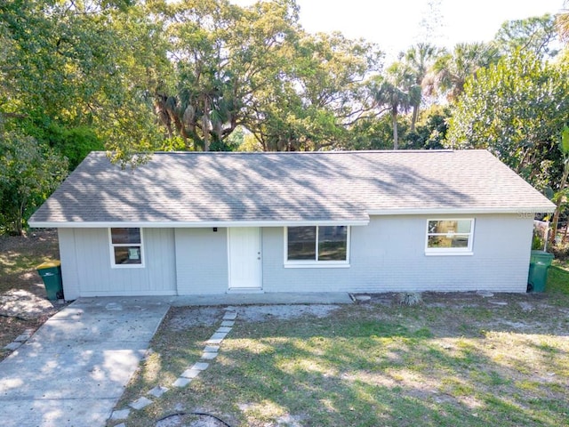 single story home with brick siding, a front lawn, roof with shingles, and driveway