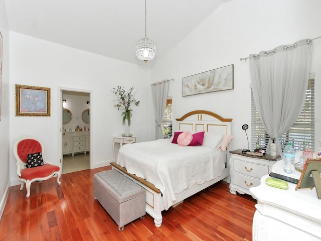 bedroom with wood finished floors, connected bathroom, an inviting chandelier, baseboards, and vaulted ceiling