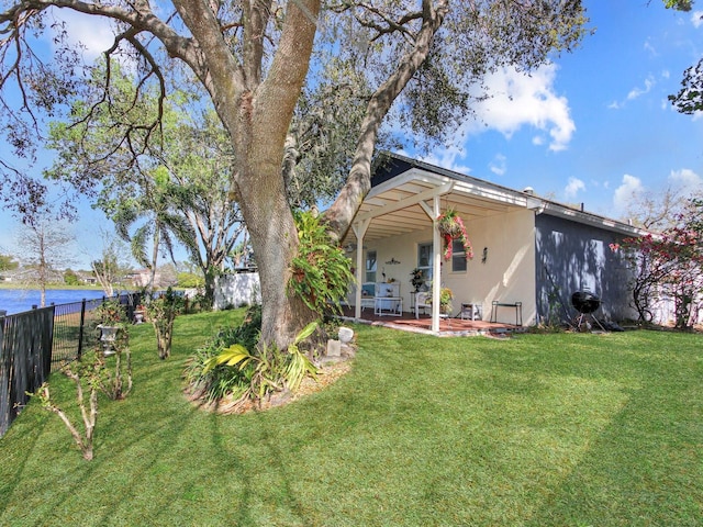 view of front of property with stucco siding, a water view, a patio, fence, and a front yard