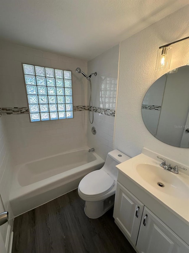 bathroom featuring toilet, wood finished floors, a textured wall, vanity, and  shower combination