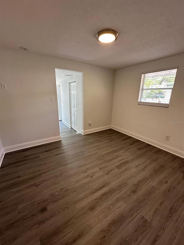 spare room with baseboards, dark wood-style flooring, and a textured ceiling