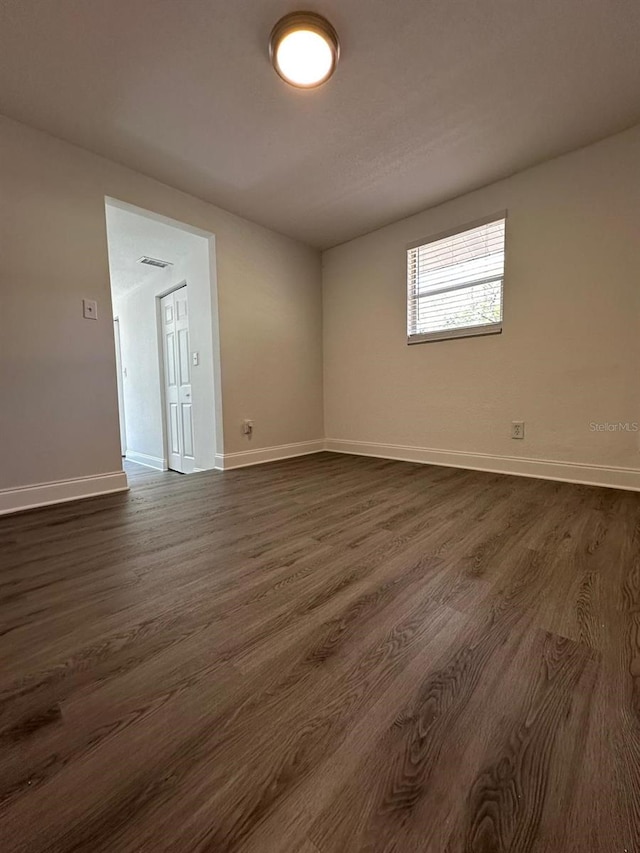 spare room featuring visible vents, baseboards, and dark wood-style floors