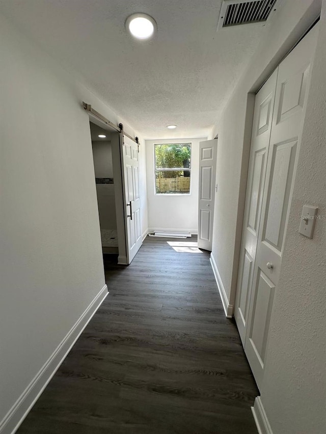 hallway with visible vents, a barn door, dark wood-type flooring, and baseboards