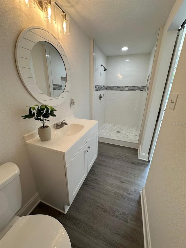 bathroom featuring toilet, vanity, a tile shower, wood finished floors, and a textured ceiling