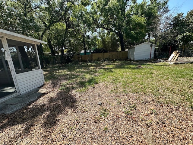 view of yard featuring a storage unit, an outbuilding, a fenced backyard, and a sunroom