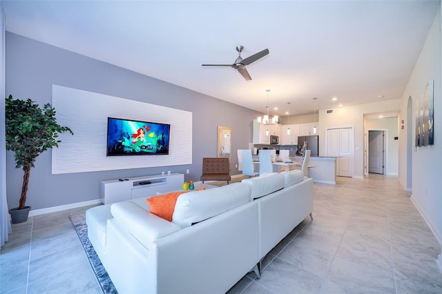 living area featuring light tile patterned floors, recessed lighting, ceiling fan with notable chandelier, and baseboards