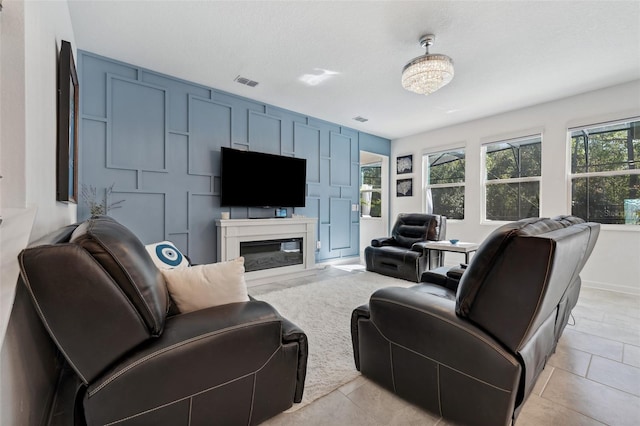 living area with a glass covered fireplace, a decorative wall, light tile patterned flooring, and visible vents