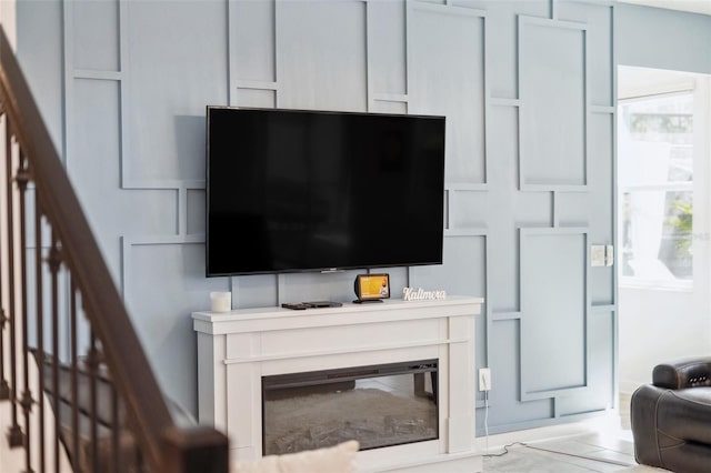 living room with stairway, a decorative wall, and a glass covered fireplace