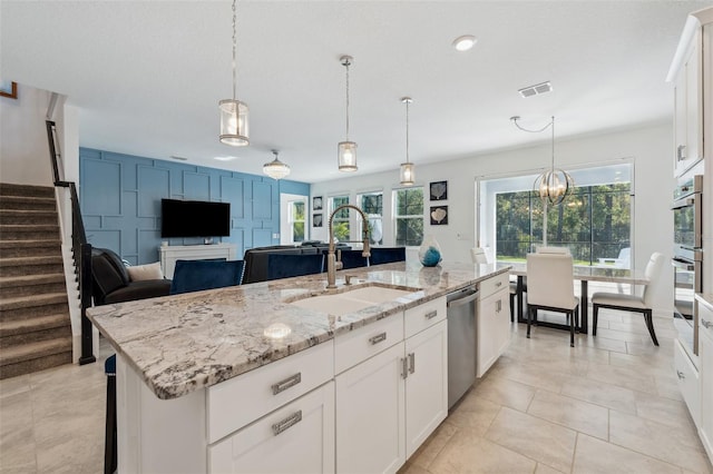 kitchen featuring visible vents, a sink, stainless steel appliances, white cabinetry, and a kitchen island with sink