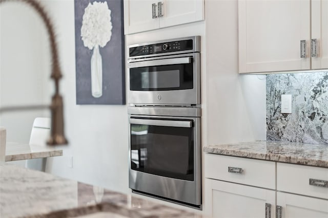 kitchen with backsplash, light stone countertops, double oven, and white cabinets