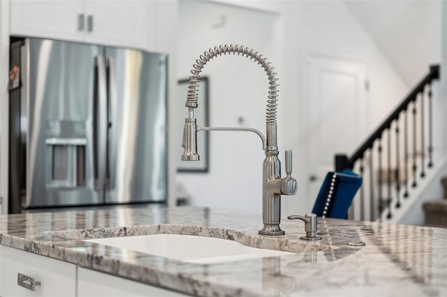 interior details with a sink, light stone countertops, white cabinetry, and stainless steel fridge with ice dispenser