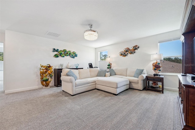 living area with plenty of natural light, light colored carpet, visible vents, and baseboards