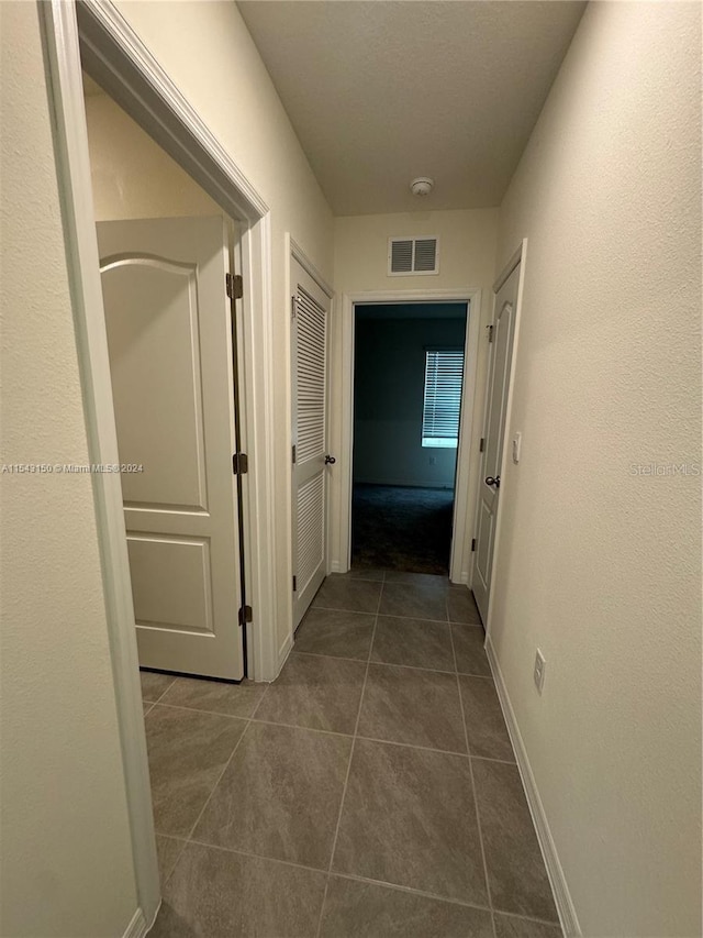 hall featuring visible vents, baseboards, and dark tile patterned flooring