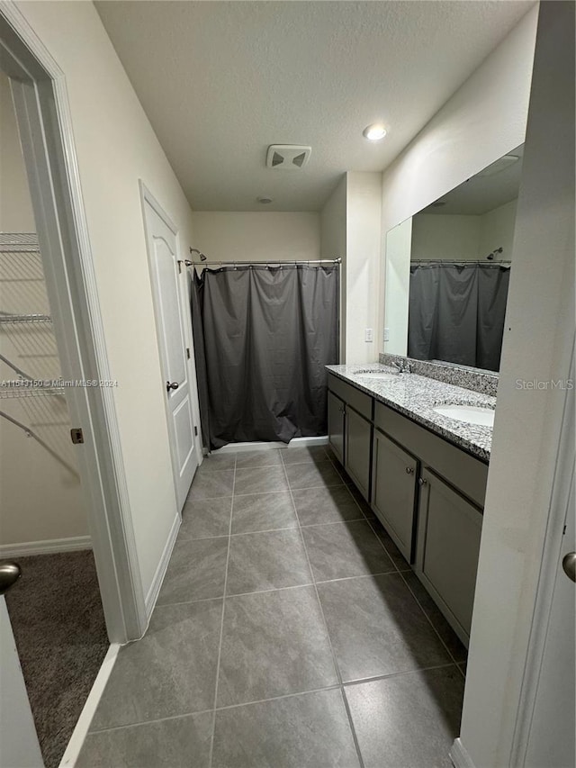 bathroom with visible vents, double vanity, a sink, tile patterned flooring, and a textured ceiling