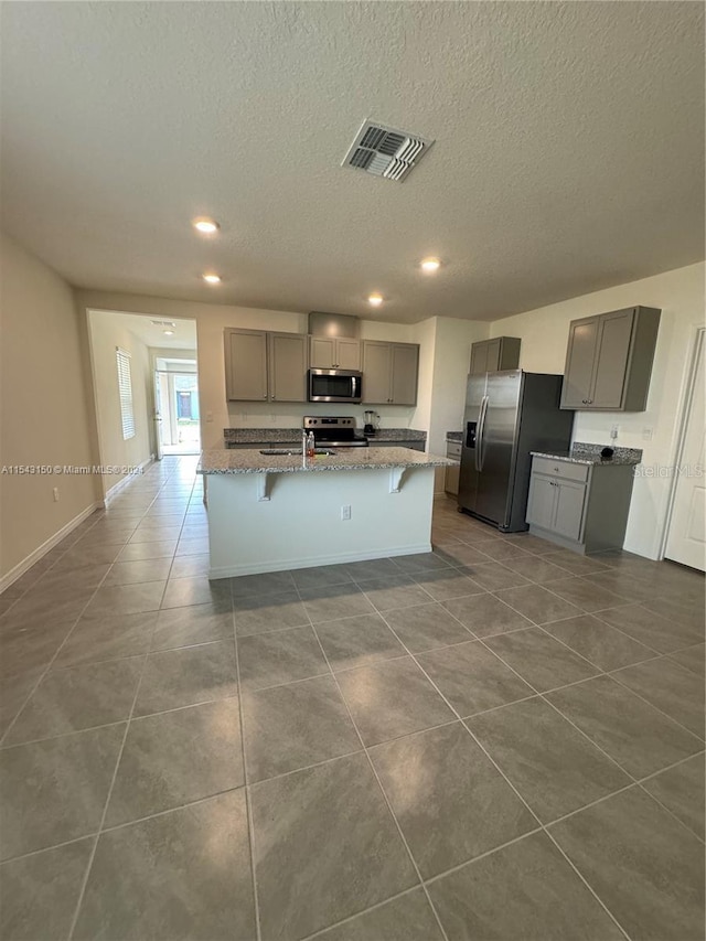 kitchen with a breakfast bar area, visible vents, dark tile patterned flooring, gray cabinets, and appliances with stainless steel finishes