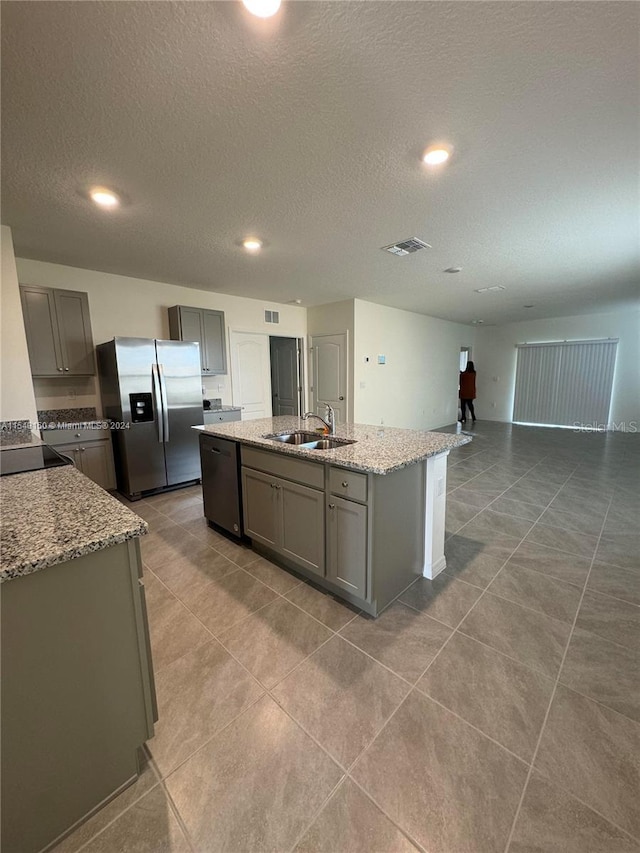 kitchen with a center island with sink, gray cabinets, a sink, stainless steel fridge, and dishwasher