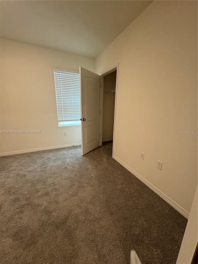 spare room featuring dark colored carpet and baseboards