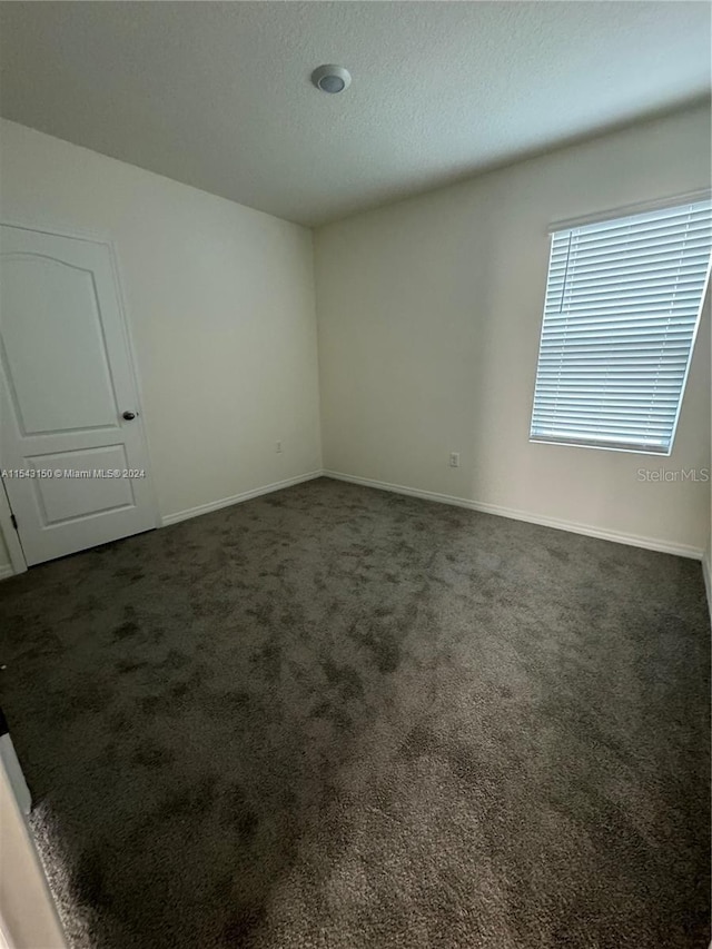 empty room with baseboards, a textured ceiling, and dark carpet