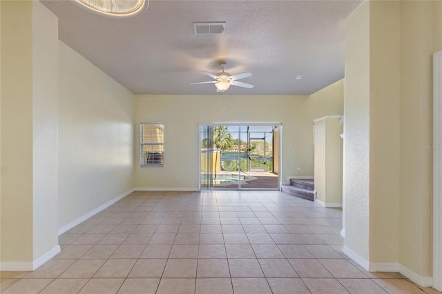 spare room featuring visible vents, baseboards, light tile patterned floors, a textured ceiling, and a ceiling fan