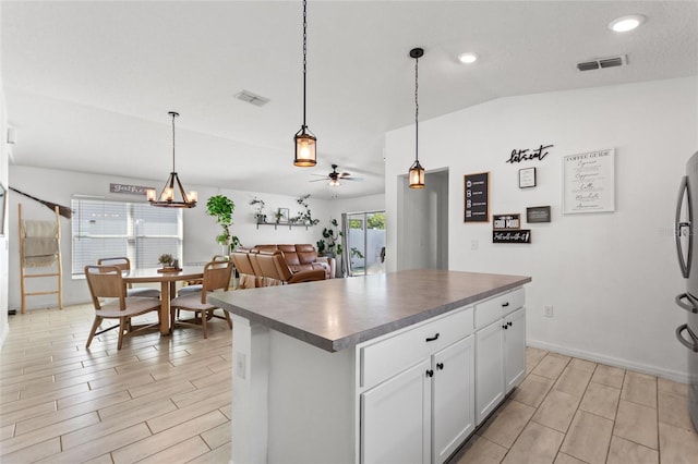 kitchen featuring visible vents, lofted ceiling, dark countertops, ceiling fan with notable chandelier, and a center island