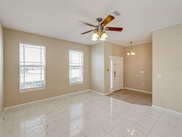 empty room with ceiling fan with notable chandelier, visible vents, marble finish floor, and baseboards