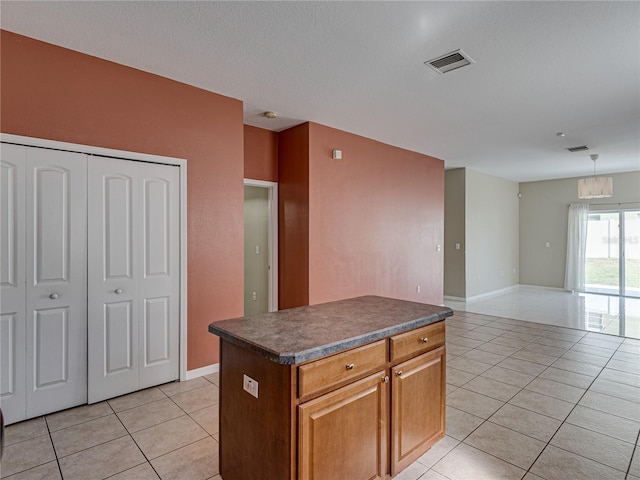 kitchen with dark countertops, visible vents, a center island, light tile patterned floors, and brown cabinets