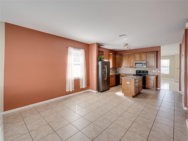 kitchen with visible vents, black appliances, a kitchen island, light tile patterned flooring, and decorative backsplash