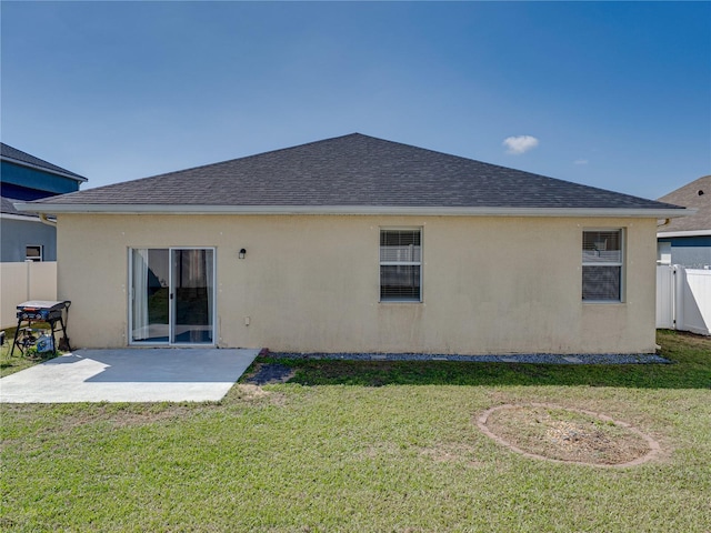 rear view of house featuring fence, a yard, a shingled roof, stucco siding, and a patio area