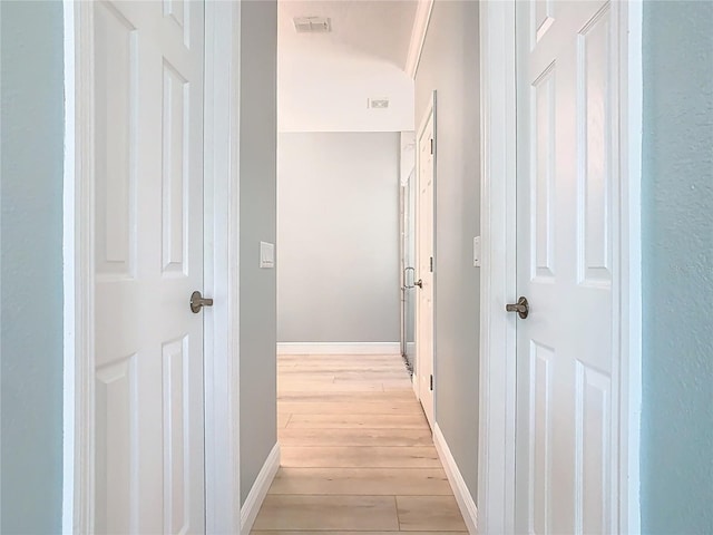 corridor featuring visible vents, baseboards, and light wood finished floors