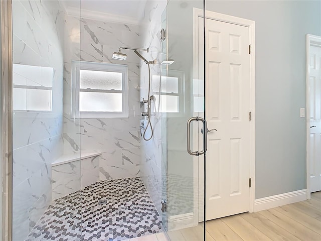 bathroom with crown molding, wood finished floors, baseboards, and a marble finish shower