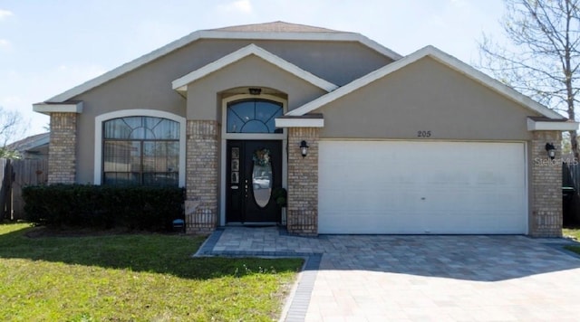 ranch-style house featuring stucco siding, a front lawn, decorative driveway, a garage, and brick siding