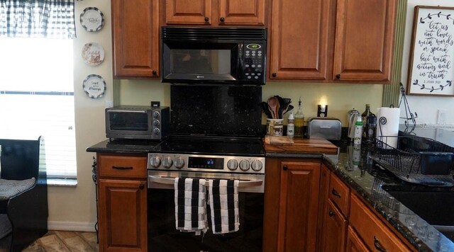 kitchen featuring a toaster, stainless steel electric range, dark stone counters, and black microwave