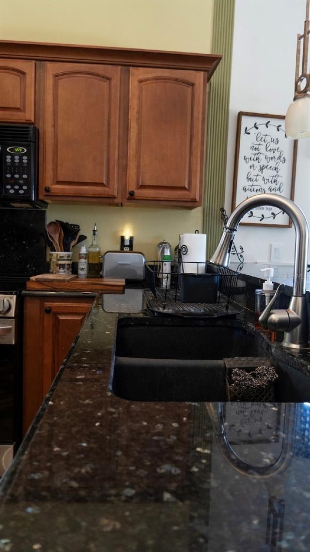 kitchen with stainless steel gas range oven, brown cabinets, a sink, dark stone counters, and black microwave