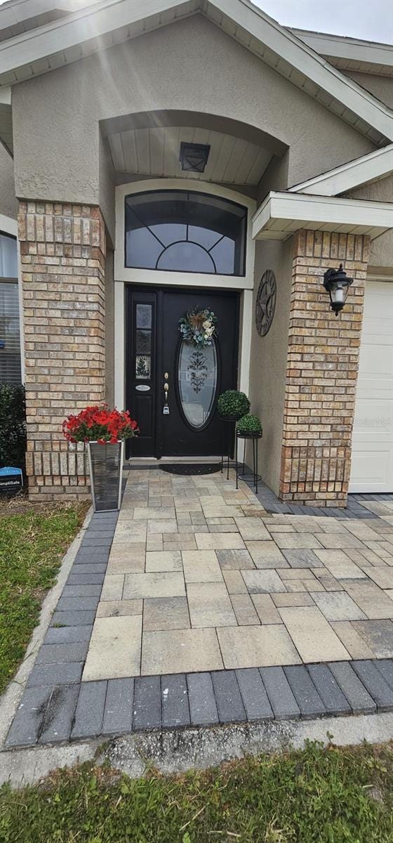 doorway to property with a garage, stucco siding, and stone siding
