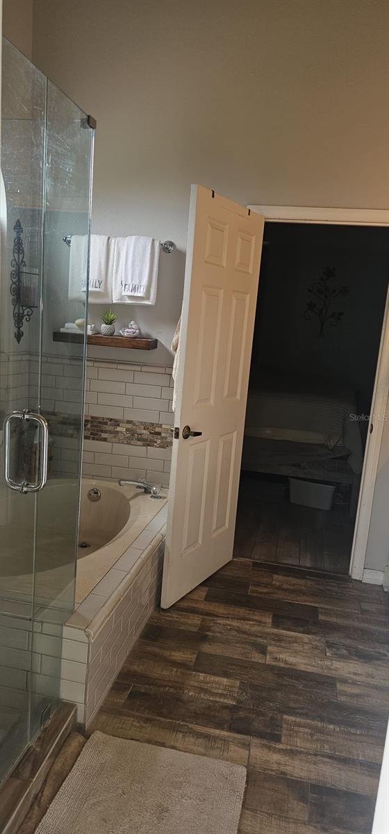 full bathroom featuring a bath, a stall shower, and wood finished floors