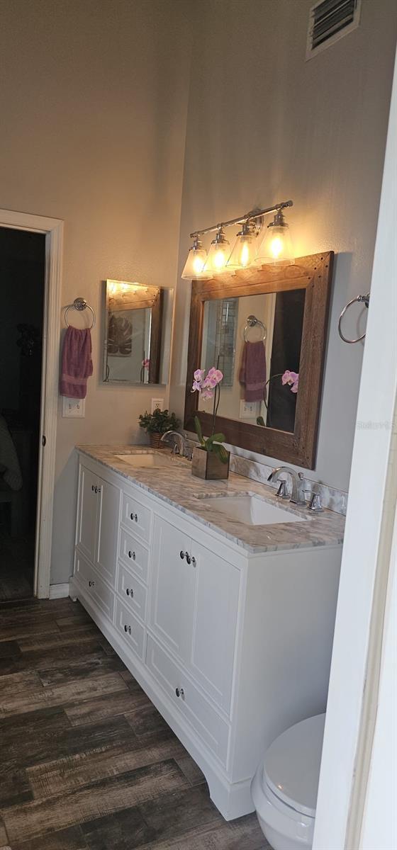full bath featuring a sink, visible vents, double vanity, and wood finished floors