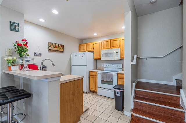 kitchen with a sink, white appliances, a peninsula, a breakfast bar area, and light countertops