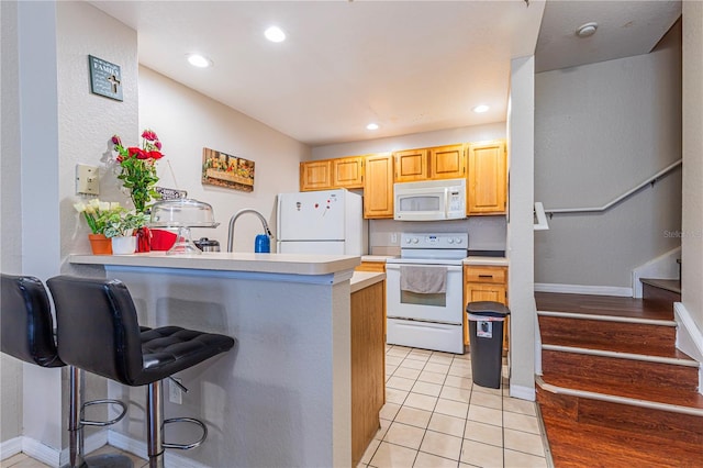 kitchen featuring white appliances, light tile patterned floors, a breakfast bar, a peninsula, and light countertops