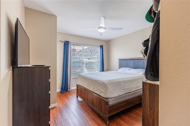 bedroom with a ceiling fan, wood finished floors, baseboards, and a textured wall