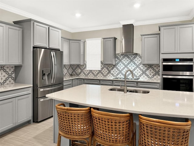 kitchen with a kitchen bar, gray cabinets, a sink, stainless steel appliances, and wall chimney exhaust hood