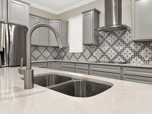 kitchen with gray cabinetry, wall chimney range hood, backsplash, crown molding, and stainless steel fridge with ice dispenser