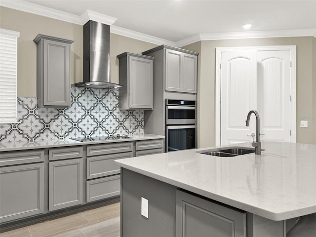 kitchen with stainless steel double oven, gray cabinetry, wall chimney range hood, and a sink