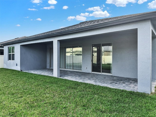 rear view of house featuring a patio area, a lawn, and stucco siding