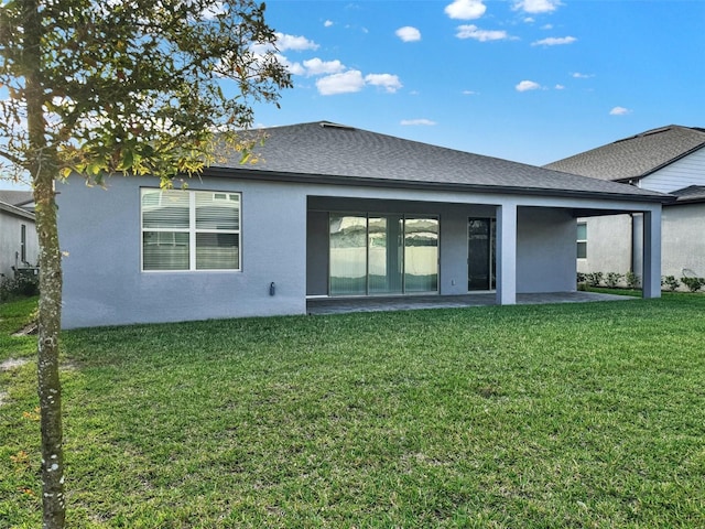 back of house with a shingled roof, a patio, a yard, and stucco siding