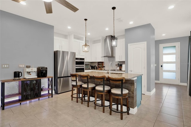 kitchen with light stone counters, a sink, appliances with stainless steel finishes, white cabinetry, and wall chimney range hood