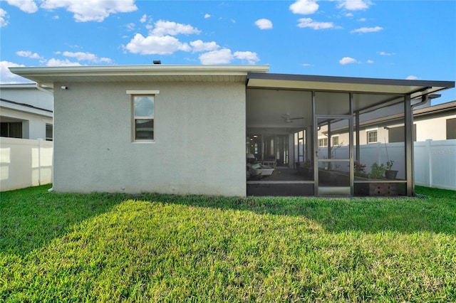 back of house with stucco siding, a sunroom, a yard, and fence