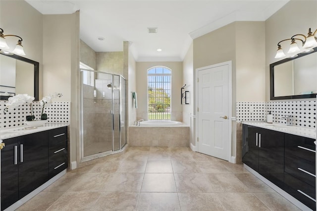 bathroom with a shower stall, crown molding, a bath, two vanities, and decorative backsplash